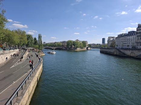 People strolling by the Seine River in Paris on a sunny day with clear skies.